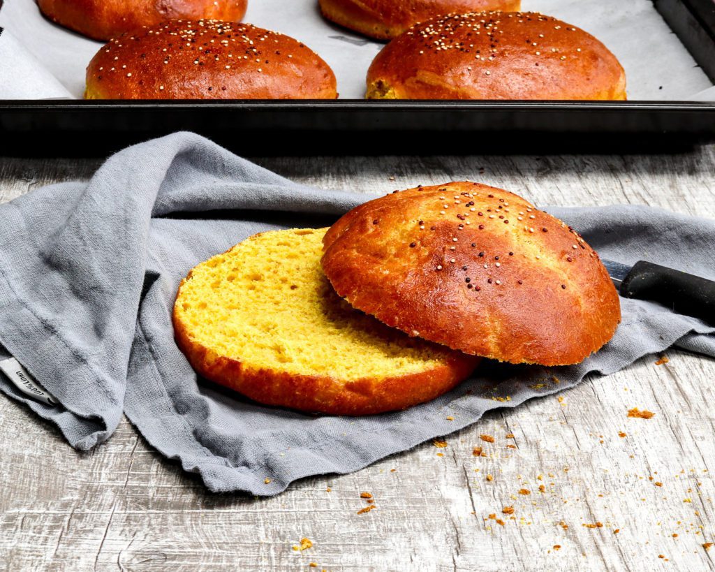 Pillowy turmeric brioche bun cut open wit baking sheet in the back