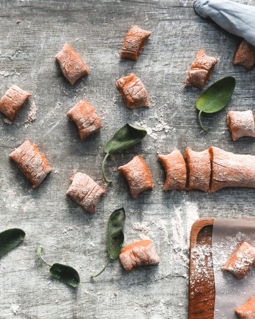 raw sweet potato gnocchi on grey surface with fresh sage leaves