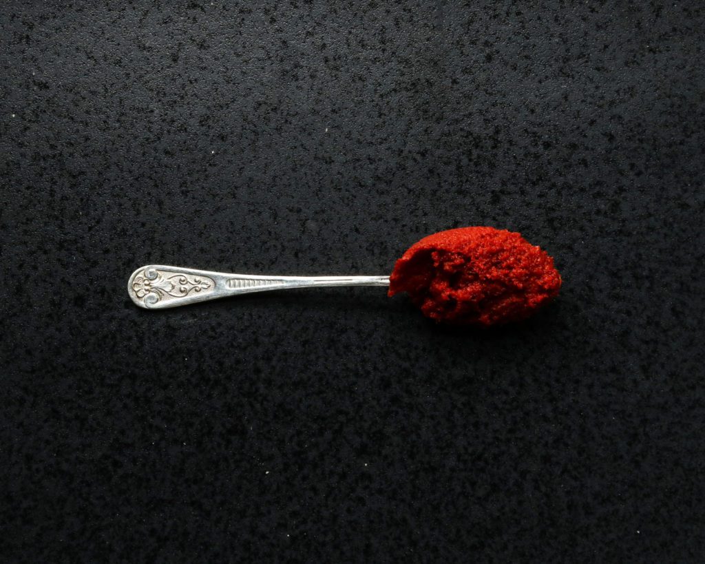 silver spoon with red curry paste on a dark stone underground