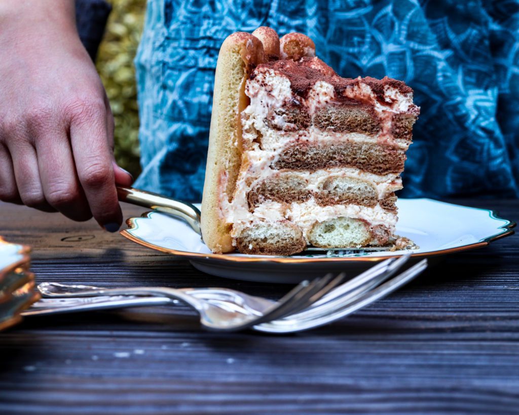 a Slice of an tiramisu cake on a white plate with someone in the background